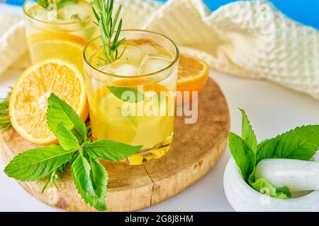 Erfrischungsgetränk im Sommer. Glas Wasser mit Orange, Minze und Rosmarin. Hausgemachte Limonade mit Eis Stockfoto