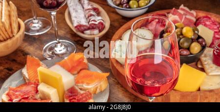 Gourmet-Wein-Vorspeisen-Panorama mit einem Glas Rosenwein, einem Käse- und Wurstbrett und Lachs-Sandwiches. Italienische Antipasti oder spanische Tapas-Panorama-Banner Stockfoto