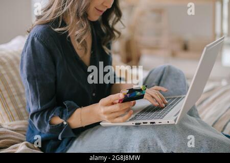 Asiatische Frau mit Kreditkarte beim Online-Shopping auf einem modernen Laptop zu Hause Stockfoto