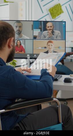 Rückansicht des behinderten gelähmten, ungültigen Managers, der mit dem Team über den Verkaufsbericht sprach, Videokonferenz im Startup-Büro hatte. Team nutzt Online-Meeting-Diskussionen über die Webcam Stockfoto