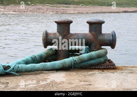 Alte rostende Stahlverankerung Poller und Hawser an einem kleinen Hafen gelegen Stockfoto