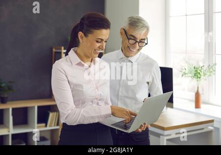 Kollegen im Büro sprechen in freundlicher Atmosphäre über Arbeitsmomente, die auf dem Laptop-Bildschirm zu sehen sind. Stockfoto