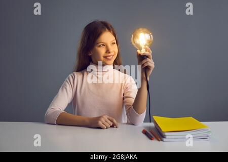 Mädchen Kind mit glühenden Glühbirne Blick auf Lampe sitzen am Schreibtisch Studio aufgenommen Stockfoto