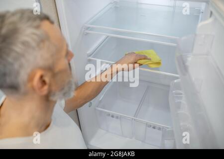 Ein grauhaariger Mann, der den Kühlschrank in der Küche putzte Stockfoto