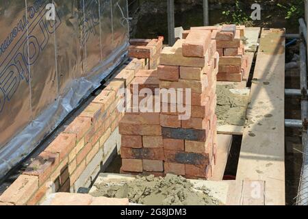 Auf Gerüsten gestapelte Ziegelsteine während des Baus der Außenwand eines neuen Bungalows in Surrey, Großbritannien Stockfoto