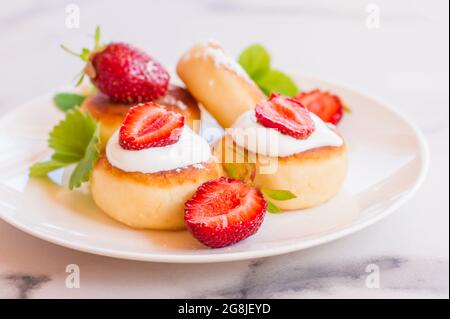 Süße Käsepfannkuchen auf dem Teller servierten Erdbeeren und Minze. Quark-Pfannkuchen, Syrniki, Ricotta-Fritten, Quark-Fritten Stockfoto