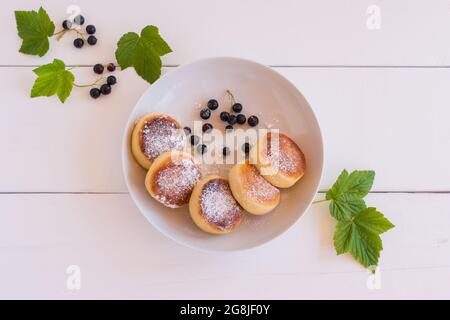 Syrniki Quark-Krapfen mit Sommerbeeren auf weißem Teller, Holztisch Hintergrund. Süßes russisches Frühstück, Käsepfannkuchen. Stockfoto