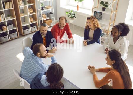 Team aus glücklichen, vielfältigen Mitarbeitern und Kollegen, die am Bürotisch sitzen und sich unterhalten Stockfoto