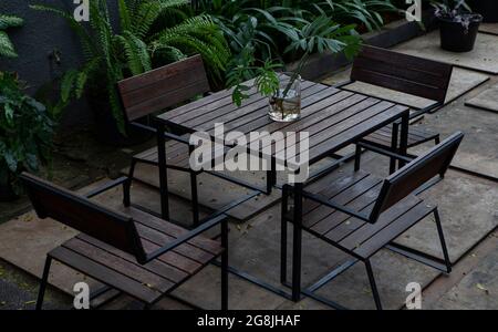 Gartentisch aus Holz mit 4 Stühlen aus Holz mit Blumen in Glastöpfen auf dem Tisch Stockfoto