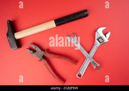 Ein Hammer, eine Zange und ein Schraubenschlüssel befinden sich auf einer roten Oberfläche Stockfoto