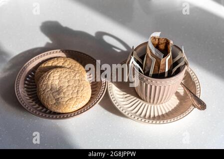 Eine Tasse heißen Kaffee mit Tropfbeutel, serviert mit Keksen in der Schale. Stockfoto