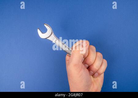 Ein Schraubenschlüssel in der Hand vor einem blauen Hintergrund Stockfoto