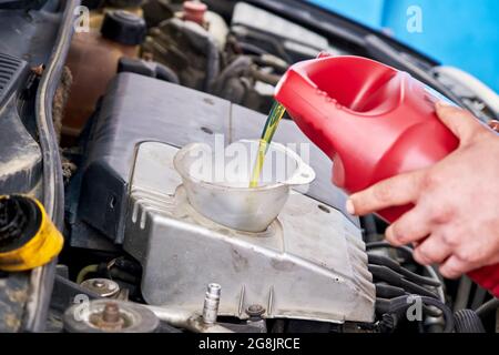 Hände eines Mechanikers, der Öl in den Automotor eingießt oder eingießt. Fahrzeugöl wechseln. Stockfoto