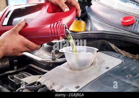 Hände eines Mechanikers, der Öl in den Automotor eingießt oder eingießt. Fahrzeugöl wechseln. Stockfoto