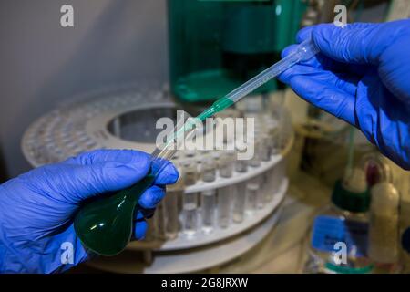Wissenschaftler analysiert CBD-Öl in einem Chemielabor. Analyse der Ionenchromatographie. Handschuhen mit Pipette und Messkolben Stockfoto