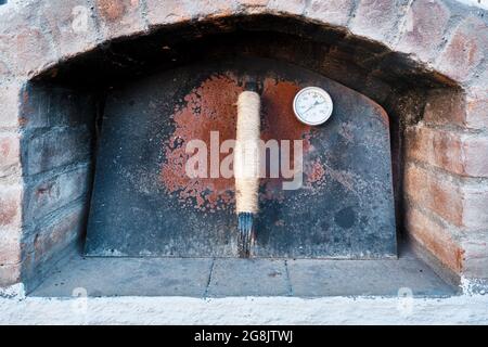 Steinofen mit geschlossener rostiger Metalltür und einem Thermometer Stockfoto