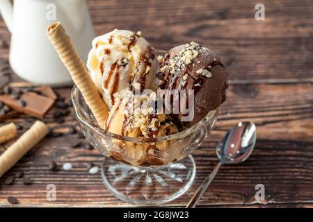 Schokolade, Rahm und Karamell-Roma-Eis in einer Glasschüssel mit Haselnuss- und Schokoladensauce darüber gegossen. Stockfoto
