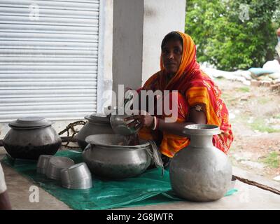 KALKUTTA, INDIEN - 30. Jun 2021: Kalkutta, Indien: Eine Inderin mittleren Alters, die Aluminium-Kochutensilien in Wasser putzt und neben ihrem h sitzt Stockfoto