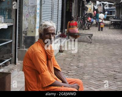 KO, INDIEN - 30. Jun 2021: Kalkutta, INDIEN: Älterer Inder (Handtrommler) trägt safranfarbene Kleidung und posiert auf der Straßenseite Stockfoto