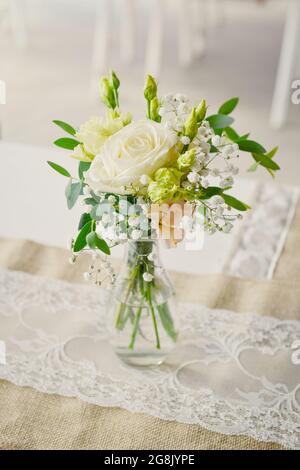 Ein kleiner Blumenstrauß mit einer weißen Rose in einer transparenten Vase auf einem Hochzeitstisch Stockfoto