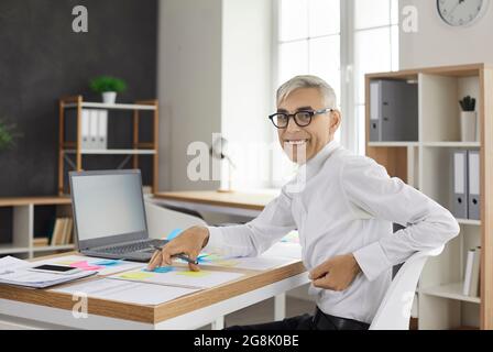 Leitender Geschäftsmann schreibt Notizen auf bunte Aufkleber, während er ein Geschäftsprojekt im Büro entwickelt. Stockfoto