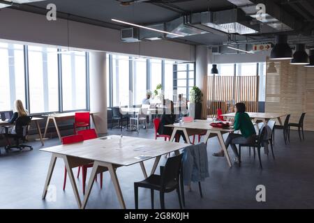 Eine vielfältige Gruppe kreativer Kollegen, die an Schreibtischen arbeiten und sich unterhalten Stockfoto