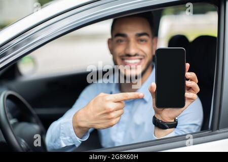 Lächelnder arabischer Geschäftsmann sitzt im Auto, zeigt Smartphone, Nachbau Stockfoto