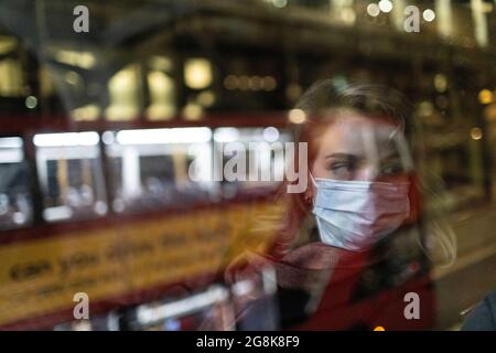 Blonde Frau mit Gesichtsmaske, die sich in der Nacht im Busfenster widerspiegelt, London, 21. Februar 2021 Stockfoto