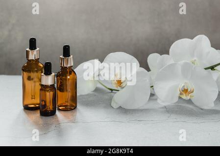 Serum oder ätherische Ölflasche Mockup mit Orchideenblüten im Hintergrund, Naturkosmetik-Hautprodukte, Home Spa in einer Tropfflasche Stockfoto