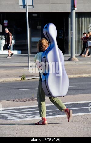 Junge Frau, die in einer Straße mit Cellogehäuse auf ihren Schultern läuft. Stockfoto