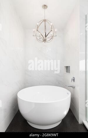 Luxuriöse Badezimmerdusche mit schwarzen runden Fliesen, eigenständige weiße Badewanne, Kronleuchter an der Decke und Chromhahn. Stockfoto
