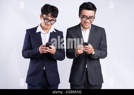 Junge vietnamesische männliche Angestellte in Anzügen, die lächeln und Telefone benutzen Stockfoto