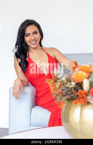 Schönheit Brünette Frau mit langen Haaren und rotem Kleid sitzt zusammen mit einem Blumenarrangement in einem farbigen bemalten Kürbis, um einen anderen zu feiern Stockfoto