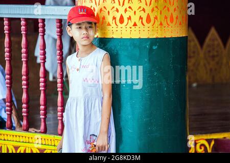 Das junge burmesische Mädchen mit roter Baseballmütze steht an der Shwedagon Pagode, Yangon, Myanmar, gegen die Säule Stockfoto