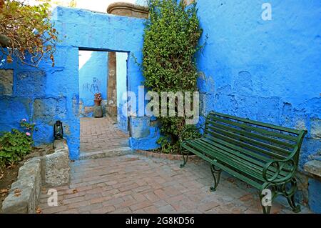Leuchtende blaue Steinmauer und grüne Bank im Kloster Santa Catalina, Arequipa, Peru Stockfoto