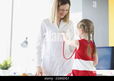 Der Arzt kommuniziert mit dem kleinen Mädchen, das Stethoskop hält Stockfoto