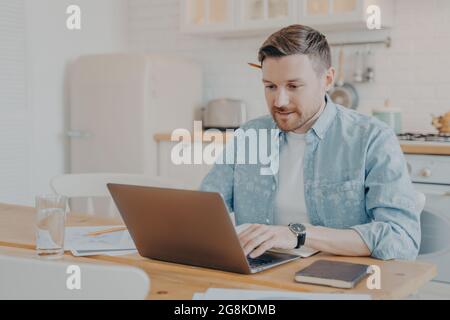 Fokussierter junger freiberuflicher Mann mit Laptop, während er am Küchentisch sitzt Stockfoto