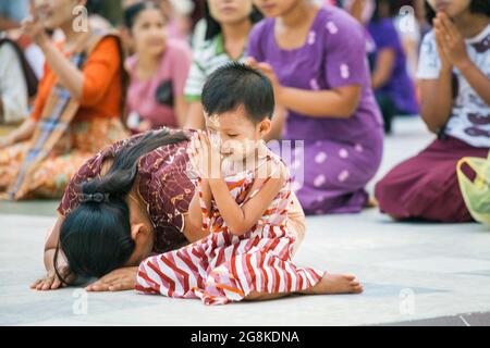 Süßes junges burmesisches Mädchen sitzt mit Thanaka-Puder in der Shwedagon Pagode, Yangon, Myanmar und betet Stockfoto