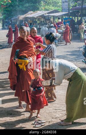 Burmesische buddhistische Novizen und ältere Mönche sammeln Almosen in einer Schale von Almosenspendern auf der Straße, Mount Popa, Myanmar Stockfoto