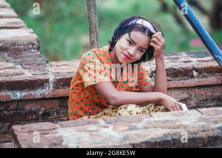 Niedliches junges burmesisches Mädchen mit Blumenbluse, leuchtend rotem Lippenstift und gelber Thanaka-Paste auf Gesichtenposen für Fotos im Tempel, Bagan, Myanmar Stockfoto