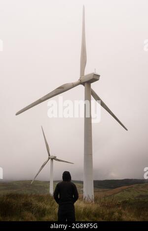 Eine geheimnisvolle Kapuzenfigur. Blick auf Windkraftanlagen auf einem Berg. An einem launischen Wintertag Stockfoto