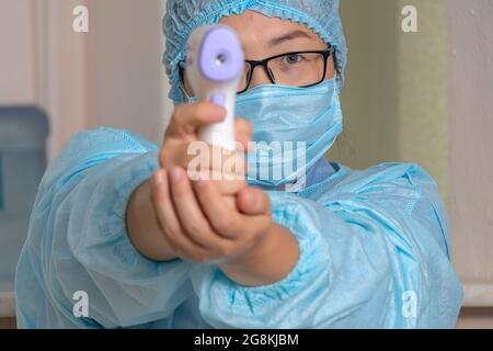 Eine Krankenschwester oder ein Arzt in einem medizinischen Einweganzug misst die Körpertemperatur des Patienten mit einem medizinischen Infrarot-Thermometer. Thermometer Pistole Isometrisch Stockfoto