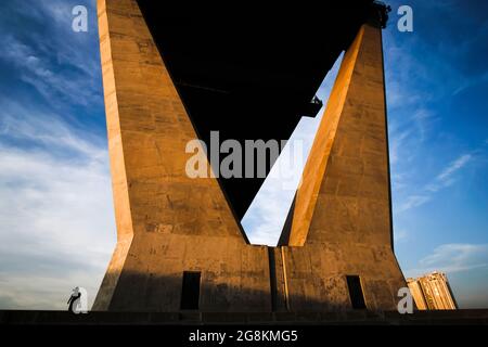 Ein Weibchen geht bei Dämmerung an den großen zwei Säulen der Hängebrücke über den Chao Phraya River vorbei. Thailand. Konzentrieren Sie sich auf zwei Säulen gebogen. Stockfoto