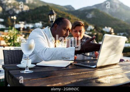 Coworking und freiberufliches Konzept. Gemischtes Rennen, schwarze Haut im mittleren Alter Mann und Frau arbeiten zusammen am Laptop, während sie auf der Cafeterrasse sitzen. Stockfoto