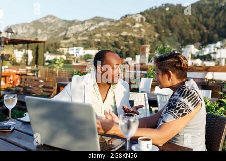 Coworking und freiberufliches Konzept. Gemischtes Rennen, schwarze Haut im mittleren Alter Mann und Frau arbeiten zusammen am Laptop, während sie auf der Cafeterrasse sitzen. Stockfoto
