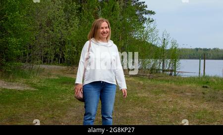 Positive Mid adult Dame tanzen in der Natur unter den Bäumen. Porträt einer Frau im Alter von 55-60 Jahren beim Entspannen im Garten. Stockfoto