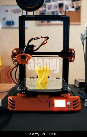 Gelbes Modell aus gelbem Kunststoff und auf einem modernen 3D-Drucker auf einem Tisch in der Werkstatt platziert Stockfoto