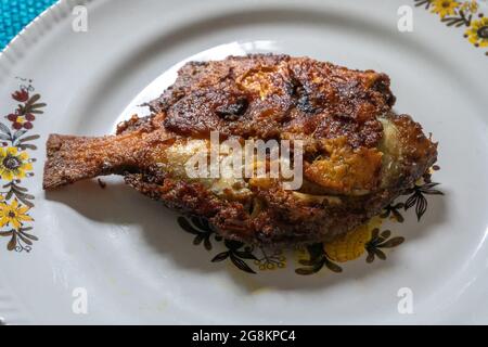 Ein gebratener Pomfret-Fisch, serviert auf einer weiß dekorierten Platte, würzige indische Gerichte. Pomfrets sind Perciforme, die zur Familie Bramidae gehören. Stockfoto