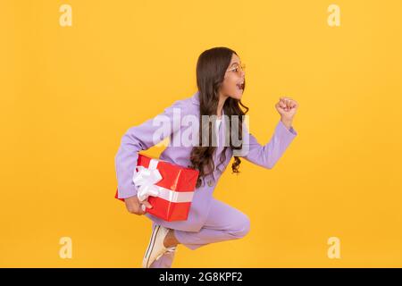 Trendy fröhlich Kind in Sonnenbrille und Anzug laufen mit Geschenk-Box zum Einkaufen Verkauf, Shopping Verkauf Stockfoto