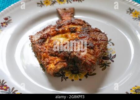 Ein gebratener Pomfret-Fisch, serviert auf einer weiß dekorierten Platte, würzige indische Gerichte. Pomfrets sind Perciforme, die zur Familie Bramidae gehören. Stockfoto